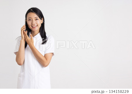スマートフォンを耳に当てて微笑む白衣姿の女性 134158229