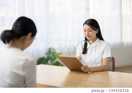 メモをとりながら笑顔で話す白衣姿の女性 メモをとりながら笑顔で話す白衣姿の女性 134158318