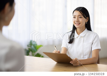 メモをとりながら笑顔で話す白衣姿の女性 メモをとりながら笑顔で話す白衣姿の女性 134158319