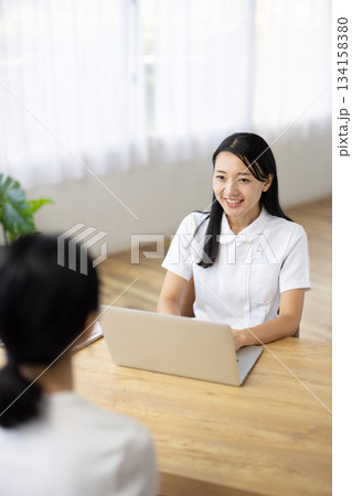 パソコンを操作しながら笑顔で話す白衣姿の女性 パソコンを操作しながら笑顔で話す白衣姿の女性 134158380