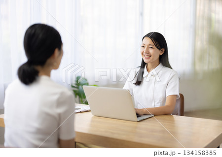 パソコンを操作しながら笑顔で話す白衣姿の女性 134158385