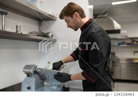 Cook operating food slicing machine during preparation 134158463