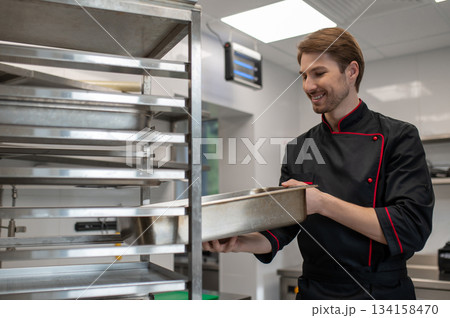 Chef inserting metal tray into rack in restaurant kitchen 134158470