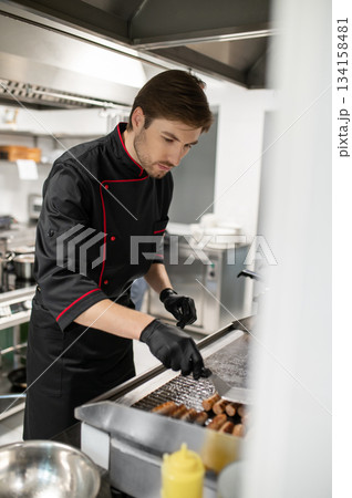 Cook preparing sausages on hot stainless steel surface in kitchen Cook preparing sausages on hot stainless steel surface in kitchen 134158481