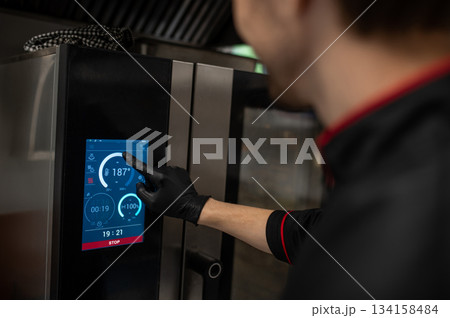 Man in black uniform setting heat on smart kitchen appliance 134158484