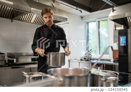 Skilled man working in restaurant standing near stove in culinary space Skilled man working in restaurant standing near stove in culinary space 134158545