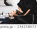 Hairdresser washing womans hair in black salon sink, creating professional beauty care moment inside modern hair studio 134158673
