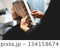 Hairdresser checking hair color of woman with professional shade chart in modern beauty salon, assessing tones and highlights with precision during color consultation 134158674