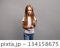 Aggressive young child girl clenching fists in emotional defensive pose, expressing frustration and defiance in studio portrait on gray background, showing intense feelings and reaction 134158675