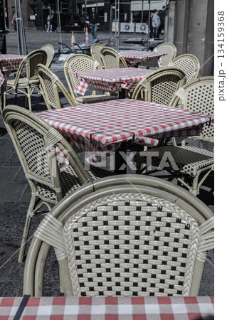 Rows of Empty tables and chairs with red and white checkered tablecloths with chairs outside a cafe on street. 134159368