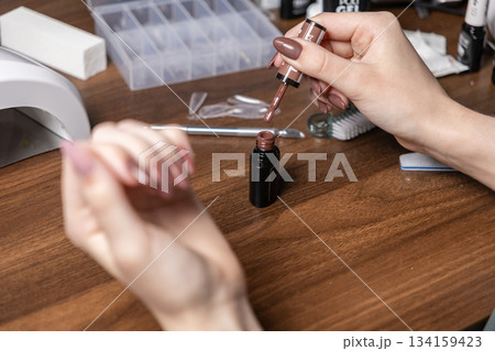 Woman performing her own personal manicure, carefully holding brown gel polish brush, demonstrating at-home self-care, beauty, and creative nail art Woman performing her own personal manicure, carefully holding brown gel polish brush, demonstrating at-home self-care, beauty, and creative nail art 134159423