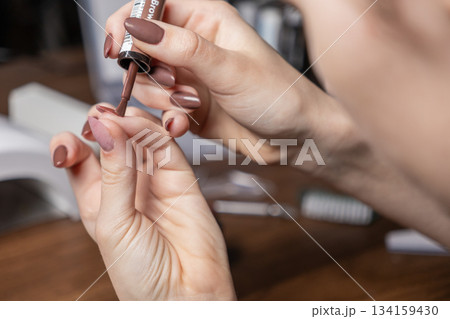 Close-up of woman's hands applying rich brown nail polish to a fingernail with an applicator brush, demonstrating a careful personal DIY manicure by oneself Close-up of woman's hands applying rich brown nail polish to a fingernail with an applicator brush, demonstrating a careful personal DIY manicure by oneself 134159430