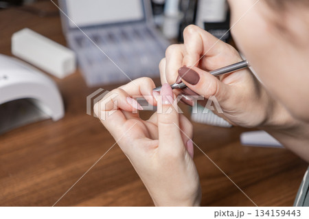Womans hands performing a manicure by oneself with cuticle pusher, emphasizing personal beauty, nail care, at-home treatment, and relaxing DIY routine 134159443