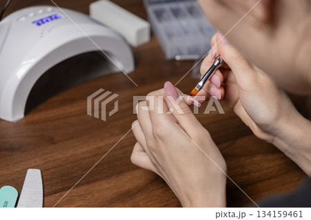 Woman applying builder gel on her fingernail with a brush, performing precise self-manicure for personal beauty and care at home Woman applying builder gel on her fingernail with a brush, performing precise self-manicure for personal beauty and care at home 134159461