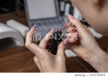 Young woman diligently applying polygel from a tube for a professional manicure by herself, creating elegant nail extensions at home for beauty Young woman diligently applying polygel from a tube for a professional manicure by herself, creating elegant nail extensions at home for beauty 134159463