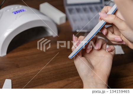 Woman's hands carefully filing long pink gel nails at home, performing a DIY manicure with professional tools, promoting self-care and beauty routine Woman's hands carefully filing long pink gel nails at home, performing a DIY manicure with professional tools, promoting self-care and beauty routine 134159465