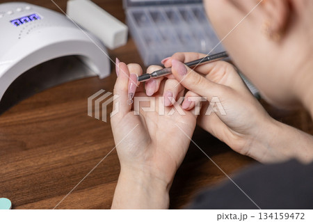 Woman's hands applying gel to nail extension upper forms during a DIY self-manicure, achieving professional personal beauty and care at home Woman's hands applying gel to nail extension upper forms during a DIY self-manicure, achieving professional personal beauty and care at home 134159472