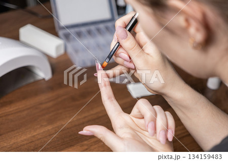 Woman carefully applying gel with a small brush onto a clear artificial nail tip for a modern DIY manicure, embodying personal self-care and home beauty Woman carefully applying gel with a small brush onto a clear artificial nail tip for a modern DIY manicure, embodying personal self-care and home beauty 134159483