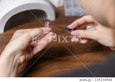 Woman applying pink polygel into a clear upper form for nail extension, performing a modern DIY manicure by herself for personal beauty and self-care 134159498