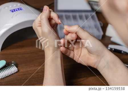 Person carefully preparing for nail extension by oneself, holding a clear upper form, utilizing a UV lamp for a modern DIY home beauty treatment 134159538