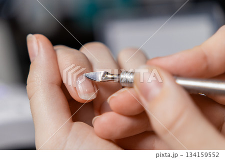 Woman's hand carefully pushing cuticles with a metal tool during a self-manicure, promoting personal beauty routine, self-care, and nail grooming at home Woman's hand carefully pushing cuticles with a metal tool during a self-manicure, promoting personal beauty routine, self-care, and nail grooming at home 134159552