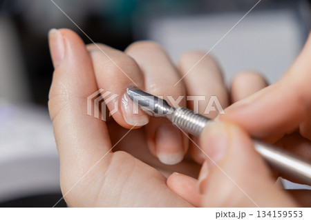 Woman performing self-manicure, meticulously pushing back cuticles on natural fingernails using a metal tool for essential personal nail care and beauty Woman performing self-manicure, meticulously pushing back cuticles on natural fingernails using a metal tool for essential personal nail care and beauty 134159553