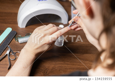 Young woman performing a meticulous DIY manicure by herself, carefully pushing back cuticles with a metal tool for personal beauty routine Young woman performing a meticulous DIY manicure by herself, carefully pushing back cuticles with a metal tool for personal beauty routine 134159555