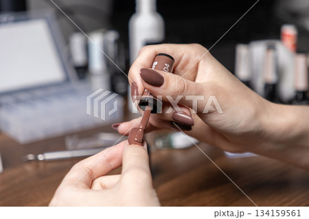 Close-up of a woman's hands meticulously applying brown nail polish to her fingernail, performing a professional self-manicure for personal grooming and beauty care Close-up of a woman's hands meticulously applying brown nail polish to her fingernail, performing a professional self-manicure for personal grooming and beauty care 134159561
