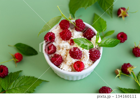 Cottage cheese with raspberries and green leaves on a green background 134160111