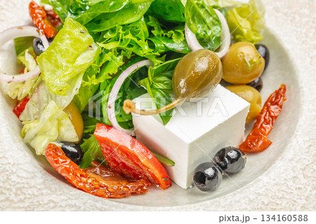 Fresh Greek salad with feta cheese, olives, caper berries, sun-dried tomatoes, and crisp greens close-up 134160588