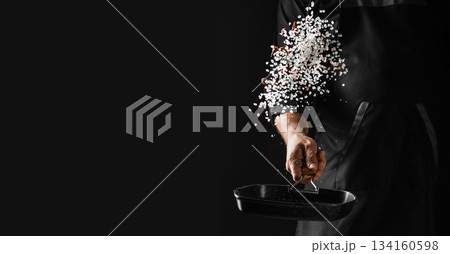 Chef sprinkling coarse salt into a hot pan on dark background with dramatic motion freeze and copy space for professional culinary advertising Chef sprinkling coarse salt into a hot pan on dark background with dramatic motion freeze and copy space for professional culinary advertising 134160598