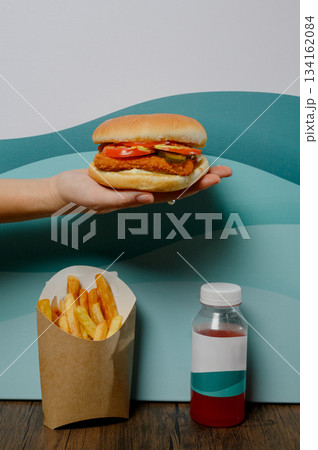 A woman's hand holds a hamburger with a patty, sauce and vegetables. 134162084