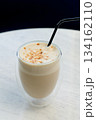 Hot milky coffee drink with foam and brown sprinkles with a black straw. 134162110