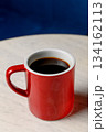 A red ceramic mug with black coffee stands on a white marble table 134162113