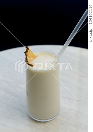 Vanilla milkshake with ice garnished with dried pineapple and a straw 134162114
