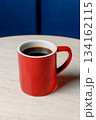 A red ceramic mug with black coffee stands on a white marble table 134162115