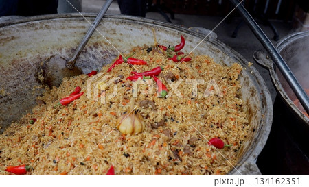 Steaming flavorful chili rice, Vendor preparing vibrant spicy rice dish, Colorful rice with chilies and garlic at festival, Aromatic spicy pilaf featuring whole chilies and garlic at local food Steaming flavorful chili rice, Vendor preparing vibrant spicy rice dish, Colorful rice with chilies and garlic at festival, Aromatic spicy pilaf featuring whole chilies and garlic at local food 134162351