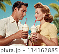 A smiling pair leans over a milkshake, sipping together in vintage 50s style. 134162885