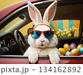 A stylish Easter bunny in sunglasses peeks from a car packed with colorful eggs. 134162892
