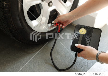 Woman using portable tire inflator with pressure gauge to check and inflate car wheel. Auto maintenance safety concept. 134163438