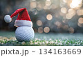 Festive golf theme with santa hat on golf ball against blurred christmas lights. Horizontal banner. Copy space. White golf ball decorated with santa hat. For golf club, sports store 134163669