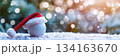 Holiday golf ball with santa hat in snowy christmas scene for holiday decor. Horizontal banner. Copy space. White golf ball decorated with santa hat, blurred background. For golf club, sports store 134163670