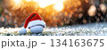 Festive golf ball with santa hat in sparkling christmas setting. Horizontal banner. Copy space. White golf ball decorated with santa hat, blurred winter background. For golf club, sports store 134163675