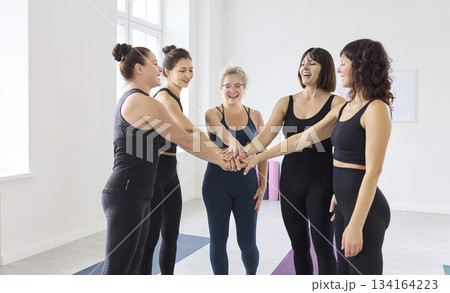 Women in a yoga studio stack hands on mats, teamwork, unity, support, connection Women in a yoga studio stack hands on mats, teamwork, unity, support, connection 134164223