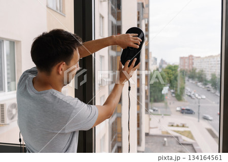 Back view of cleaning service employee mounting advanced window washing robot on skyscraper exterior, performing high-altitude maintenance with precision and safety technology. 134164561