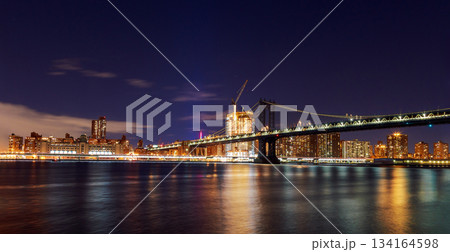 View of Manhattan Bridge New York city skyline at night with lights reflecting on water View of Manhattan Bridge New York city skyline at night with lights reflecting on water 134164598