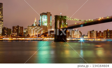 Brooklyn Bridge spans over water with city Manhattan skyline in background during night time 134164604