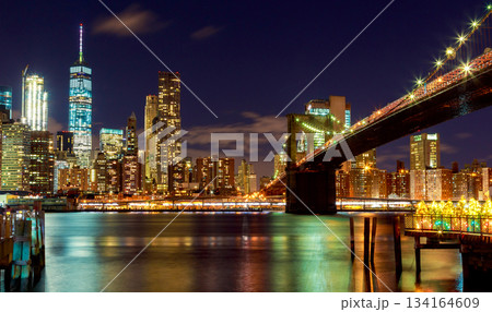 Night of Brooklyn Bridge, New York City skyline with lights shining brightly over water 134164609