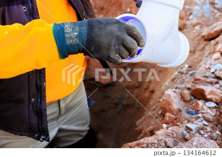Worker installs pipe in trench during plumbing project at construction site Worker installs pipe in trench during plumbing project at construction site 134164612