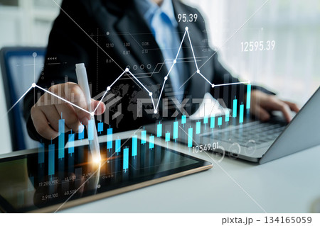 Business professional analyzing financial data with charts and graphs on a laptop and tablet in a modern office environment Scalp 134165059
